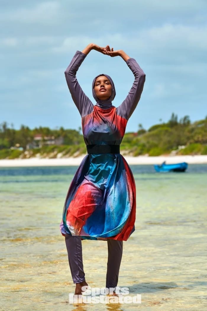 Halima Aden poses in the shallow water in a multi-colored burkini.